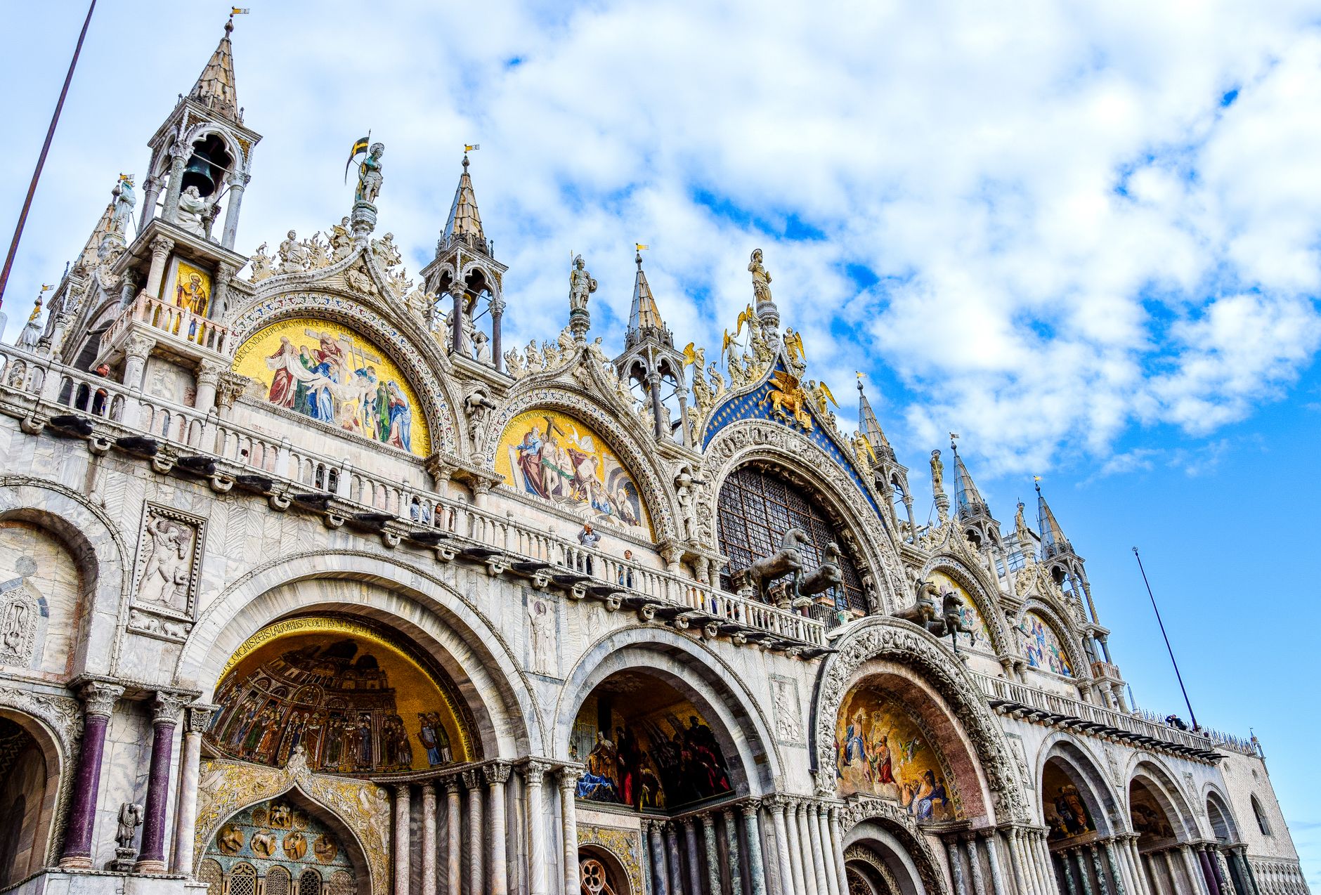 Low angle view of the ornate facade of St. Mark's Basilica under a blue sky in Venice, Italy.